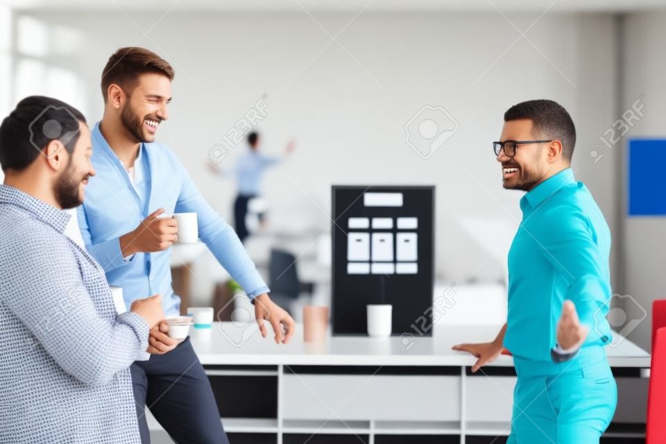 Happy diverse colleagues have fun at lunch break in office, smiling multiracial employees laugh and drinking coffee.