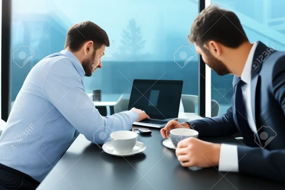 Dos hombres de negocios hablando de nuevas oportunidades sentados con una laptop en el escritorio, planificando proyectos, considerando ofertas comerciales, compartiendo ideas
