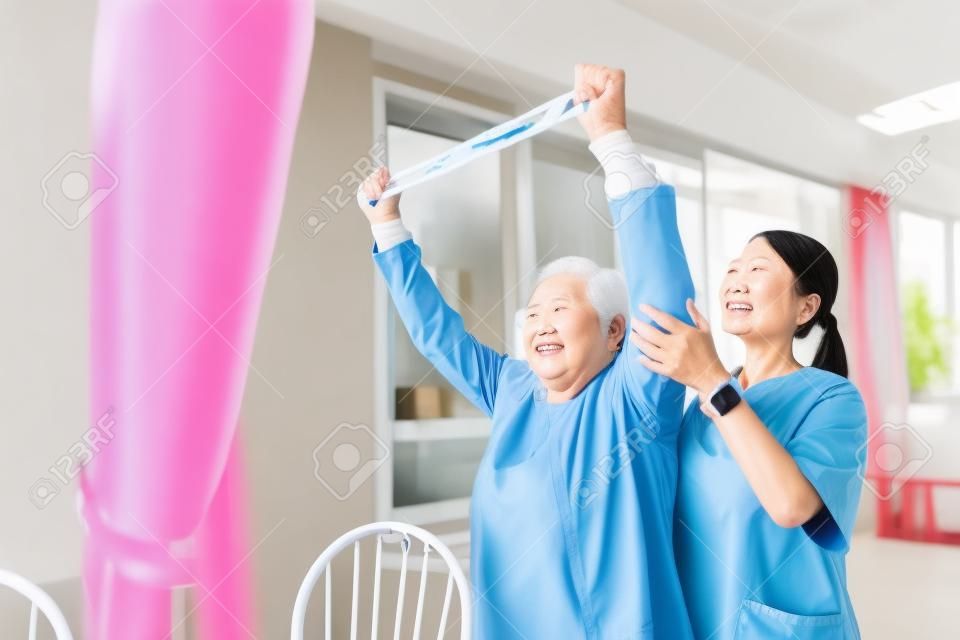L'infermiere che indossa lo scrub si esercita con una donna asiatica anziana utilizzando l'esercizio della fascia di resistenza per il paziente anziano nel trattamento fisioterapico. concetto di assistenza sanitaria domiciliare e casa di cura.