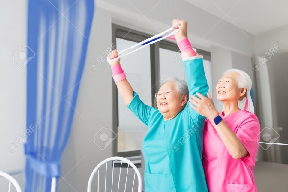 L'infermiere che indossa lo scrub si esercita con una donna asiatica anziana utilizzando l'esercizio della fascia di resistenza per il paziente anziano nel trattamento fisioterapico. concetto di assistenza sanitaria domiciliare e casa di cura.