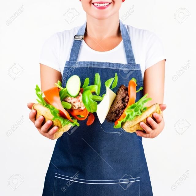 Chef mujer en un delantal de mezclilla con volar sabrosa hamburguesa casera de ingredientes naturales frescos en sus manos sobre un fondo blanco. Lugar para el texto.