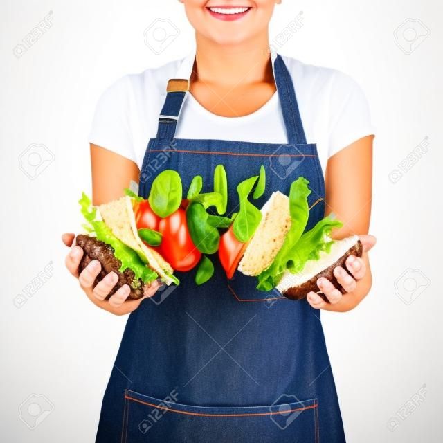 Chef mujer en un delantal de mezclilla con volar sabrosa hamburguesa casera de ingredientes naturales frescos en sus manos sobre un fondo blanco. Lugar para el texto.