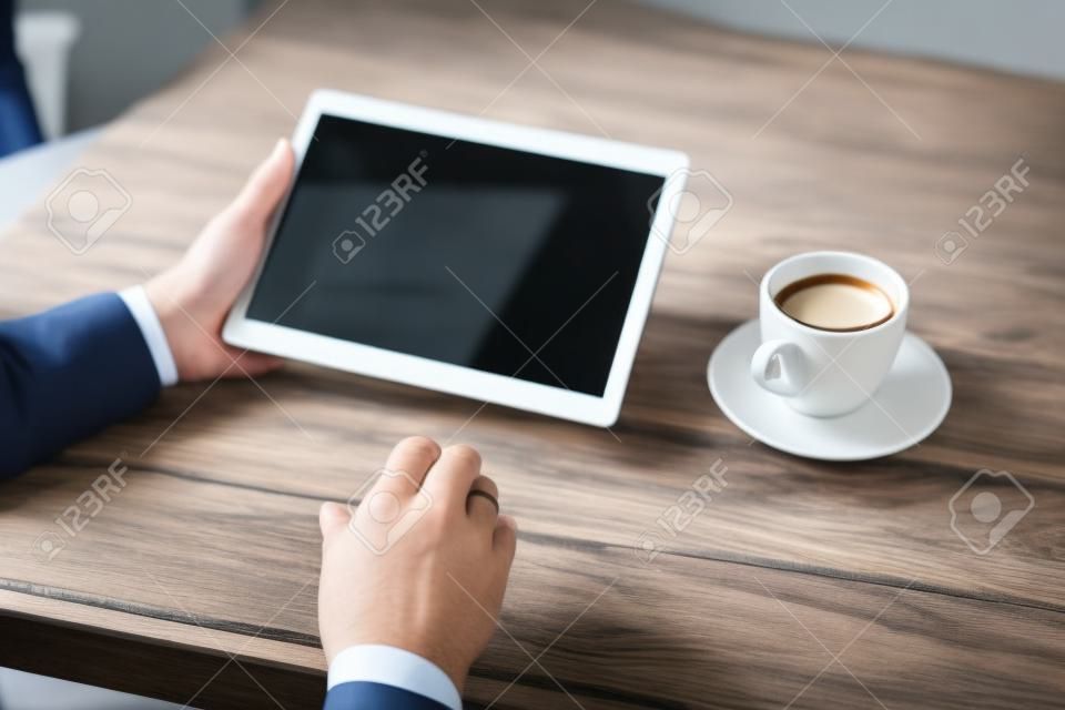 man businessman in suit using a digital tablet holding it in the office on the background of wooden table with Cup of coffee