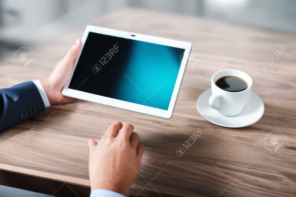 man businessman in suit using a digital tablet holding it in the office on the background of wooden table with Cup of coffee
