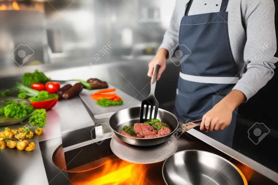 Cropped close up photo of young man fry meat pan kitchen cuisine restaurant dish supper gourmet indoors