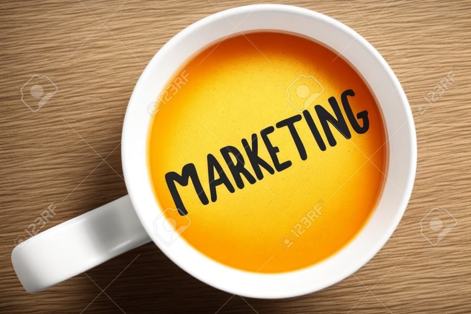 Handschrift Text schreiben Marketing. Konzept bedeutet Werbung für den Verkauf von Produkten einer Firma, um etwas geschriebenen Schwarzen Tee in weißem Cup einfarbigen Hintergrund zu fördern. Ansicht von oben.