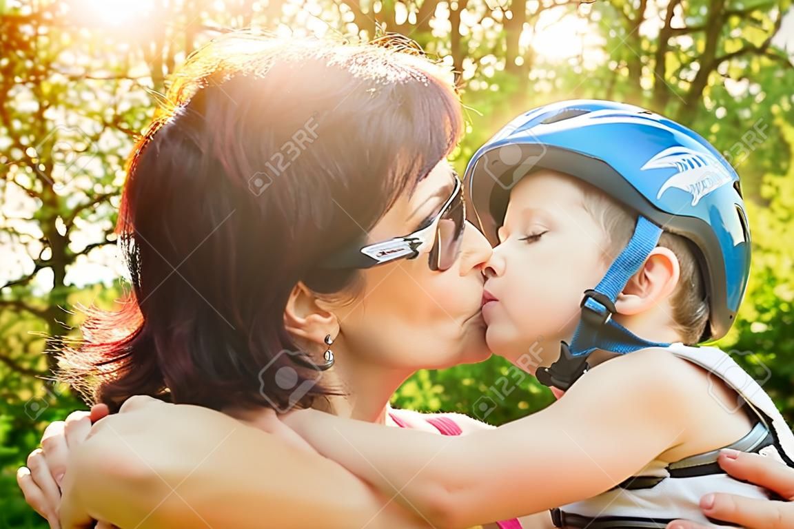 La madre bacia il suo figlio con il casco in bicicletta all'aperto