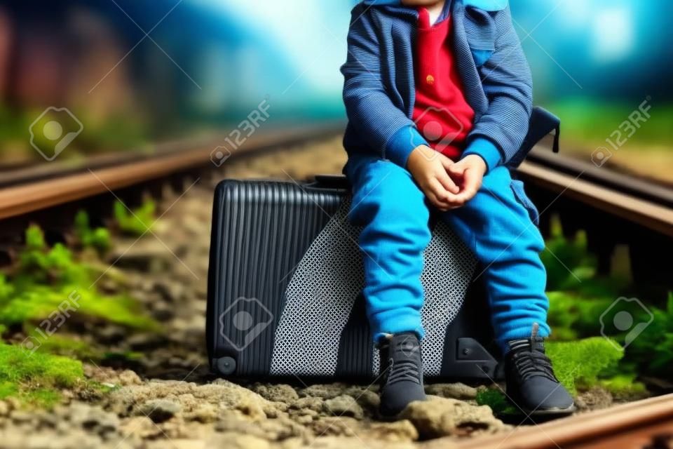 Petit garçon avec valise sur chemin de fer à l'extérieur. Concept de voyage