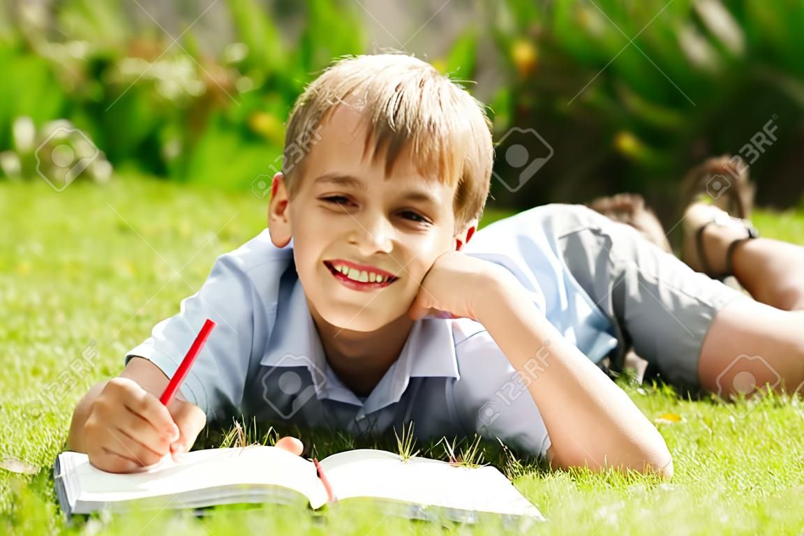 Portrait of a boy lying on the grass with a book in the park 
