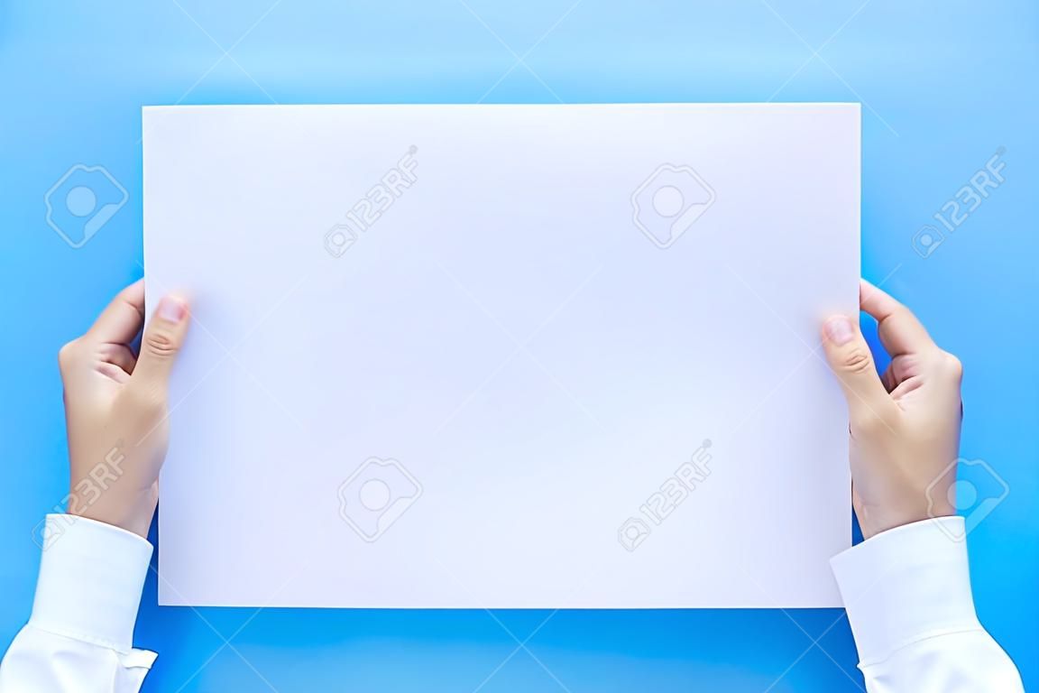Schließen Sie die Hände, die leeres weißes leeres Briefpapier im A4-Format für Flyer oder Einladungsmock-up isoliert auf blauem Hintergrund halten.