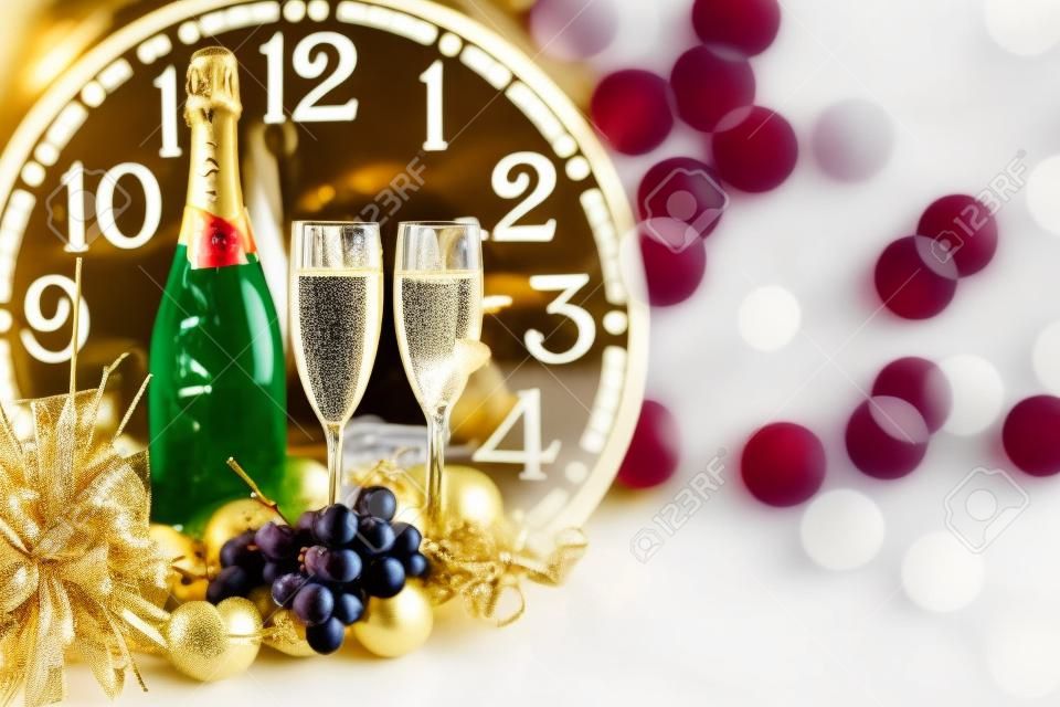 シャンパンのボトル、グラス2杯、ブドウ、装飾品をトレイに置き、時計を背景に新年を祝う