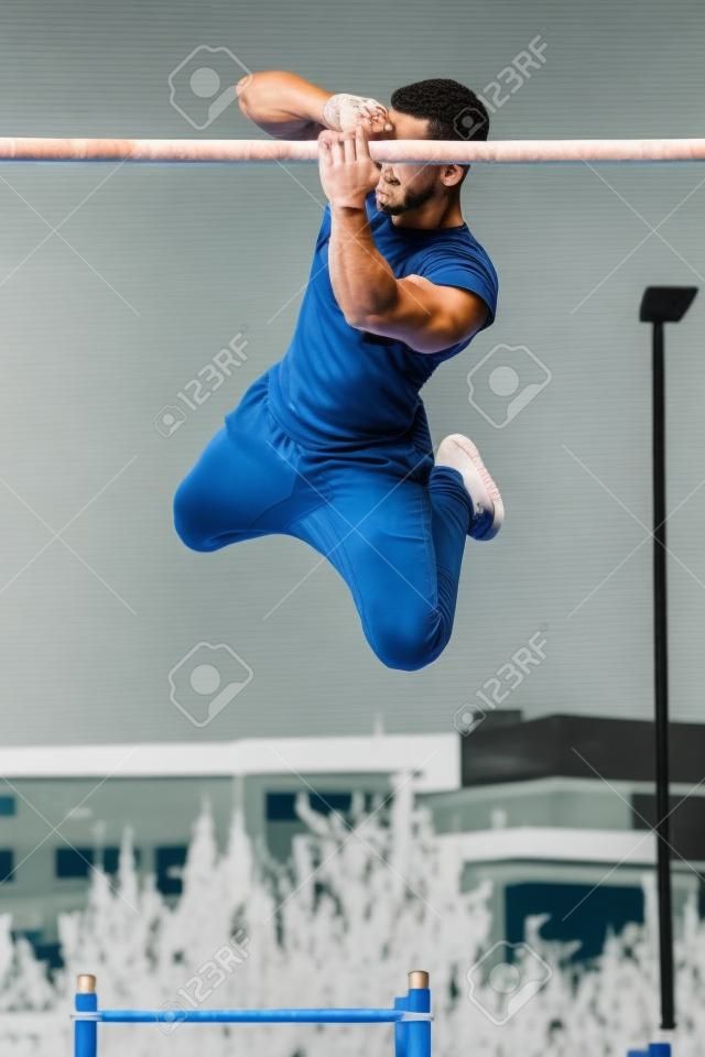 Junger athletischer Mann, der Gymnastik mit Drehungen an Stangen in einem Calisthenics-Fitnessstudio im Freien macht