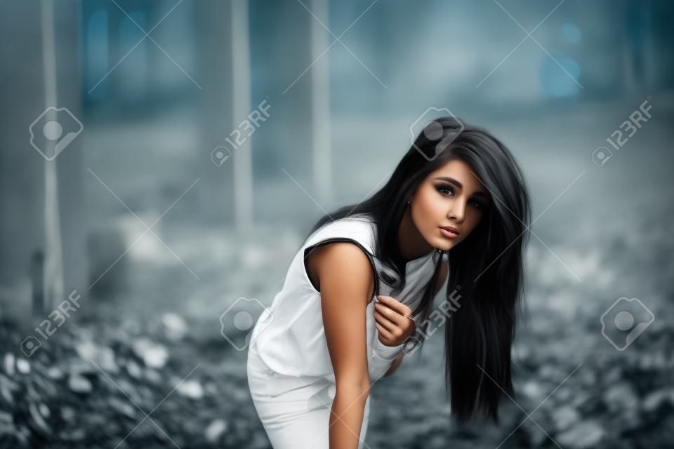 Portrait of young cute brunette girl wearing on black leather pants and white blouse posed on abandoned place.