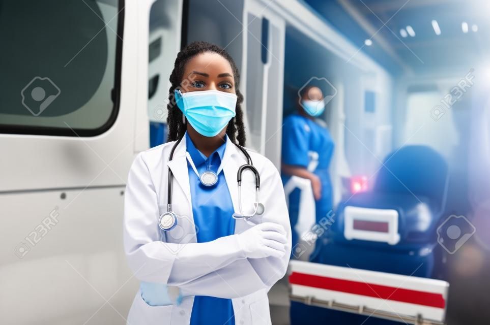 African american kobieta sanitariusz w twarzy maski medyczne stojące przed samochodem pogotowia.