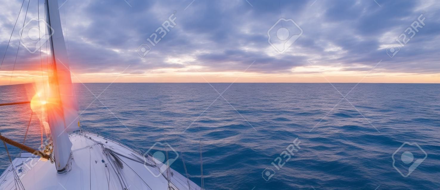 Weiße Schaluppe manipulierte Yacht, die bei Sonnenuntergang segelt. Klarer Himmel nach dem Sturm. Blick vom Deck auf Bug, Mast, Segel. Transport, Reise, Kreuzfahrt, Sport, Erholung, Freizeit, Rennen, Regatta
