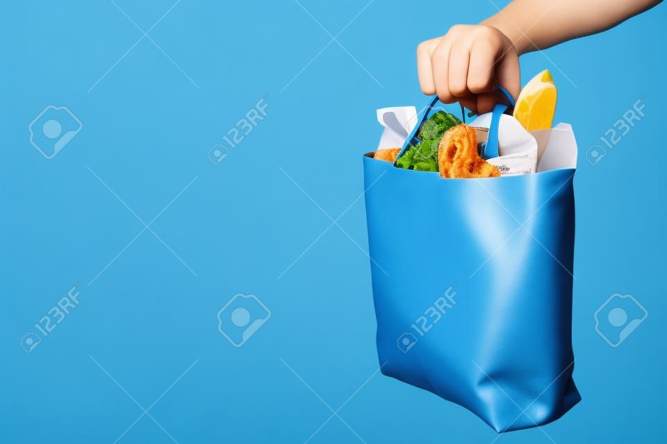 Hand holds bag with food on blue background