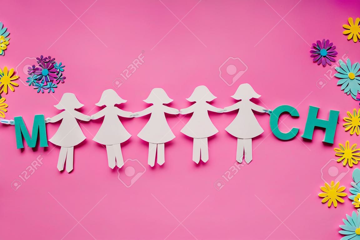 Paper doll chain, colorful little flowers and march made from colorful wooden letters on pink background