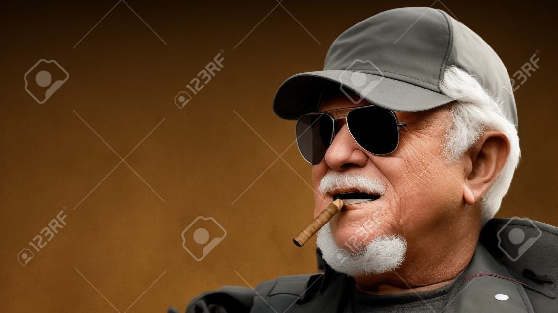Portrait of confident elderly man wearing protective clothing in sunglasses with a cigar against the background of old concrete walls