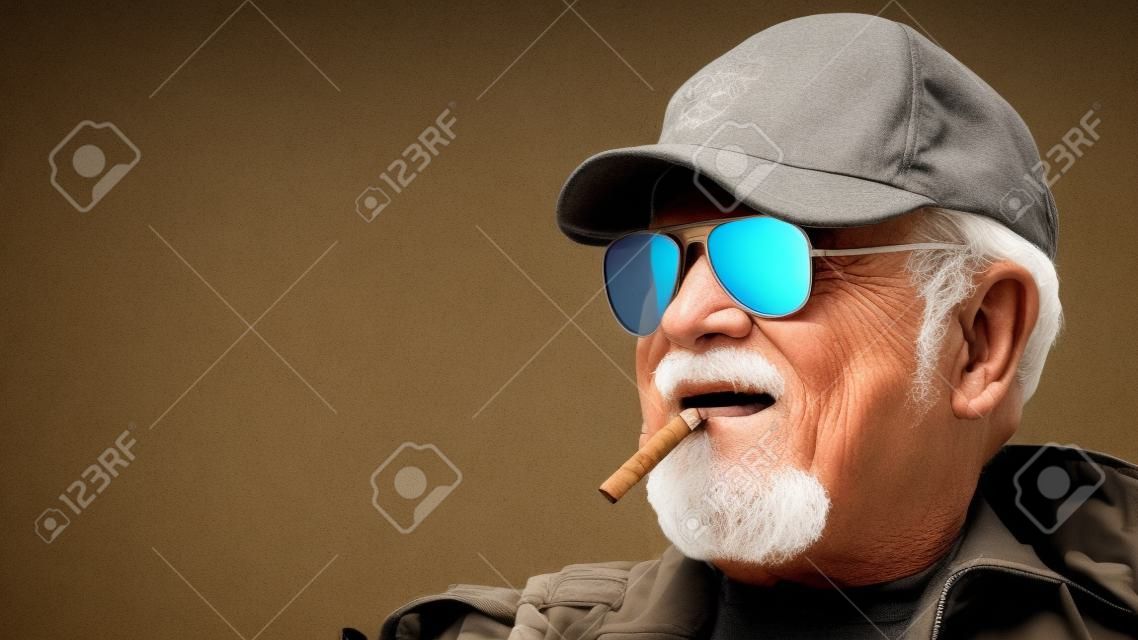 Portrait of confident elderly man wearing protective clothing in sunglasses with a cigar against the background of old concrete walls