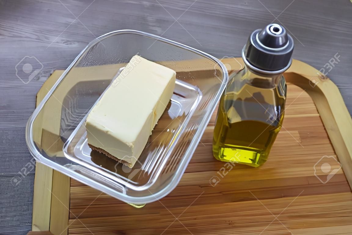 Uma pequena garrafa de azeite e copos com manteiga na mesa com uma toalha de mesa cinza
