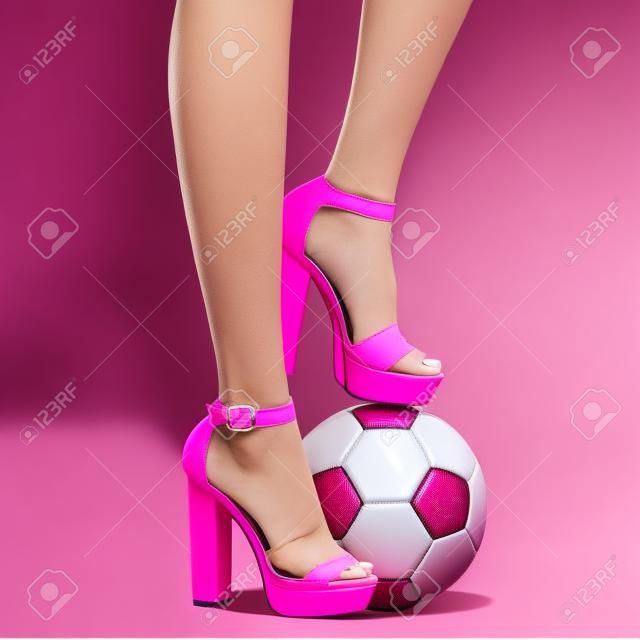 Piernas de mujer en sandalias de tacón rosa y balón de fútbol