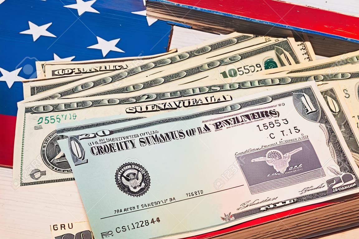 Pila di 20 banconote da un dollaro con assegno illustrativo del pagamento dello stimolo del coronavirus sulla bandiera degli Stati Uniti