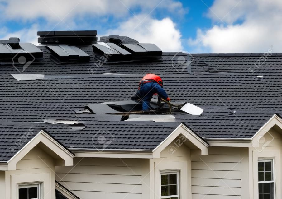 Dachdecker entfernen die alten Dachziegel, bevor sie sie durch neue Schindeln auf dem Dach eines Stadthauses ersetzen