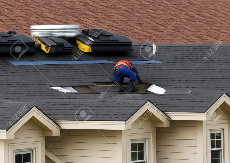 Dachdecker entfernen die alten Dachziegel, bevor sie sie durch neue Schindeln auf dem Dach eines Stadthauses ersetzen