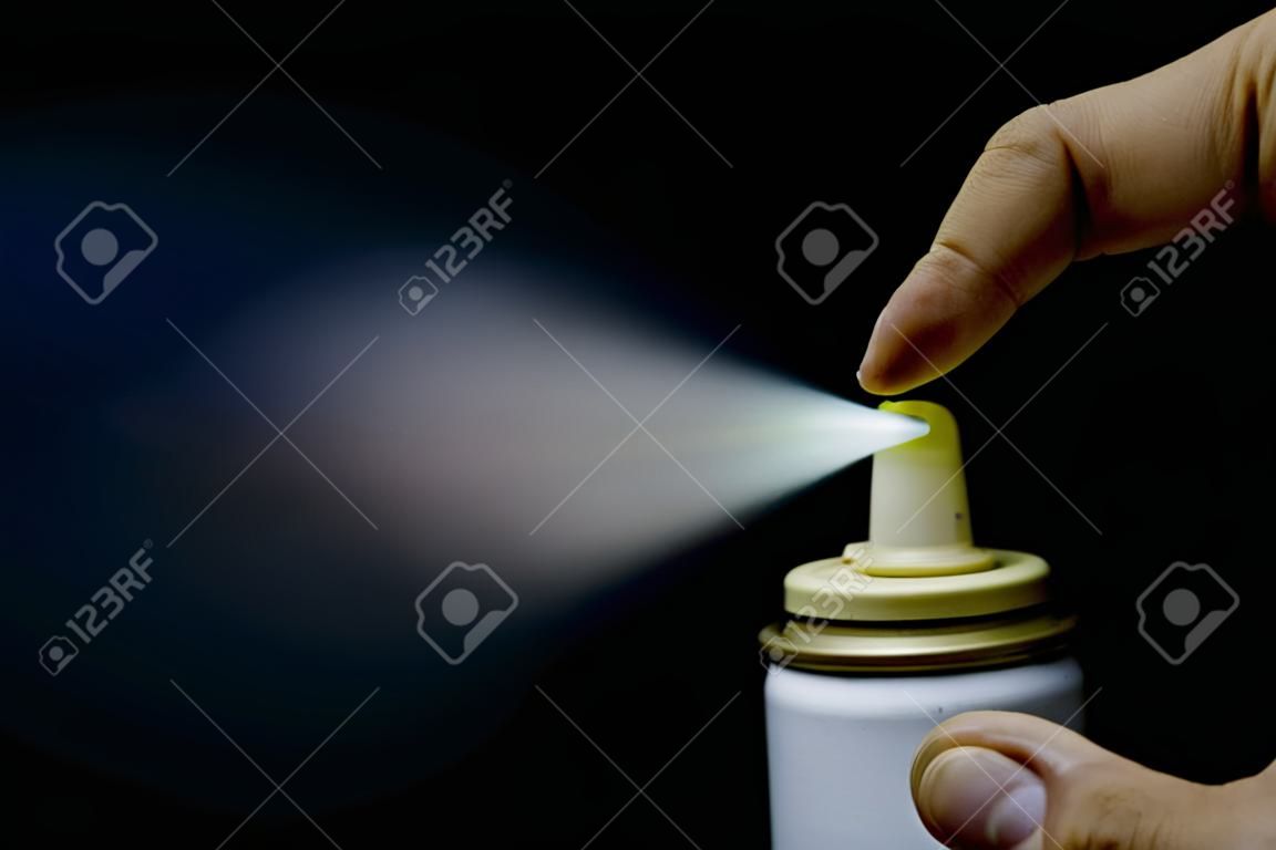 Close up view of a man spraying, A spray can in a hand on a black background Close-up
