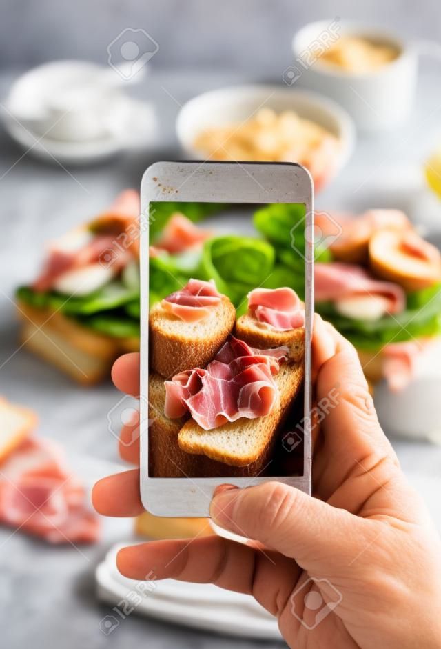 Man photographing toast sandwiches with prosciutto