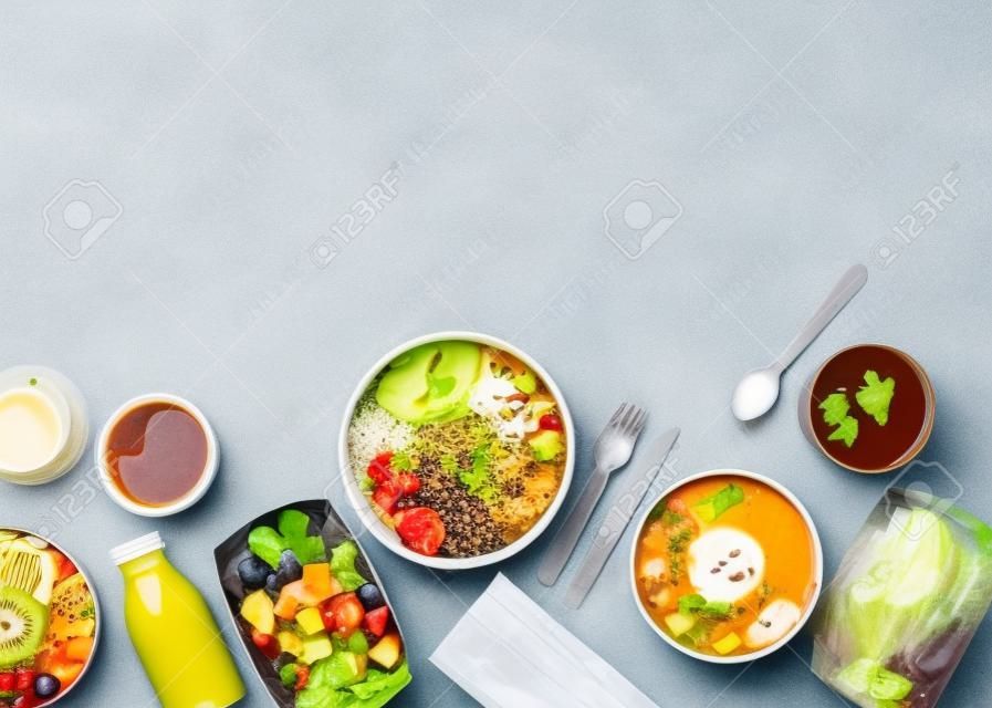 Healthy take away food and drinks in disposable eco friendly paper containers on gray background, top view. Fresh salad, soup, poke bowl, buddha bowl, fruits, coffee and juice.