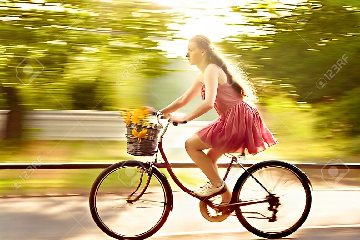 Bewegungsunschärfe. junge Frau in einem Kleid reitet auf einem Fahrrad in einem Sommerpark. Aktive Menschen. Draußen