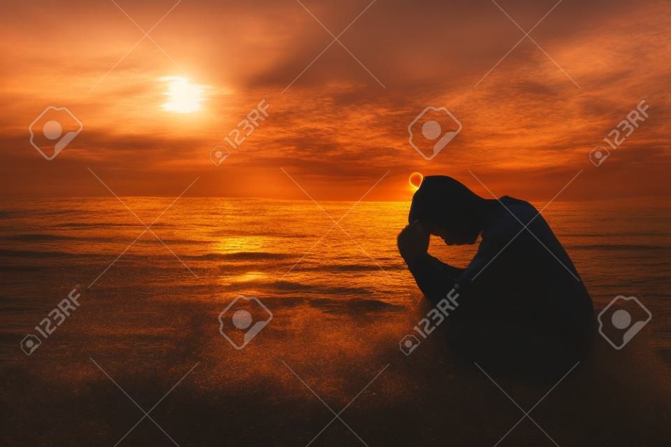 Молодой человек молится Богу во время заката на берегу моря