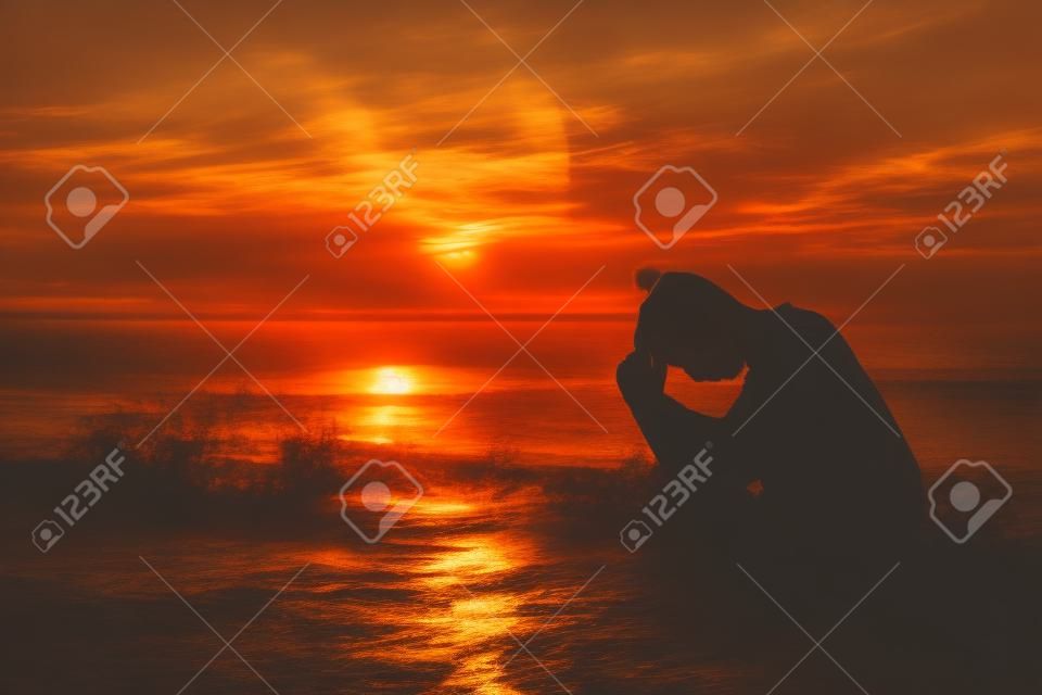 年輕男子在海邊向上帝祈禱在日落