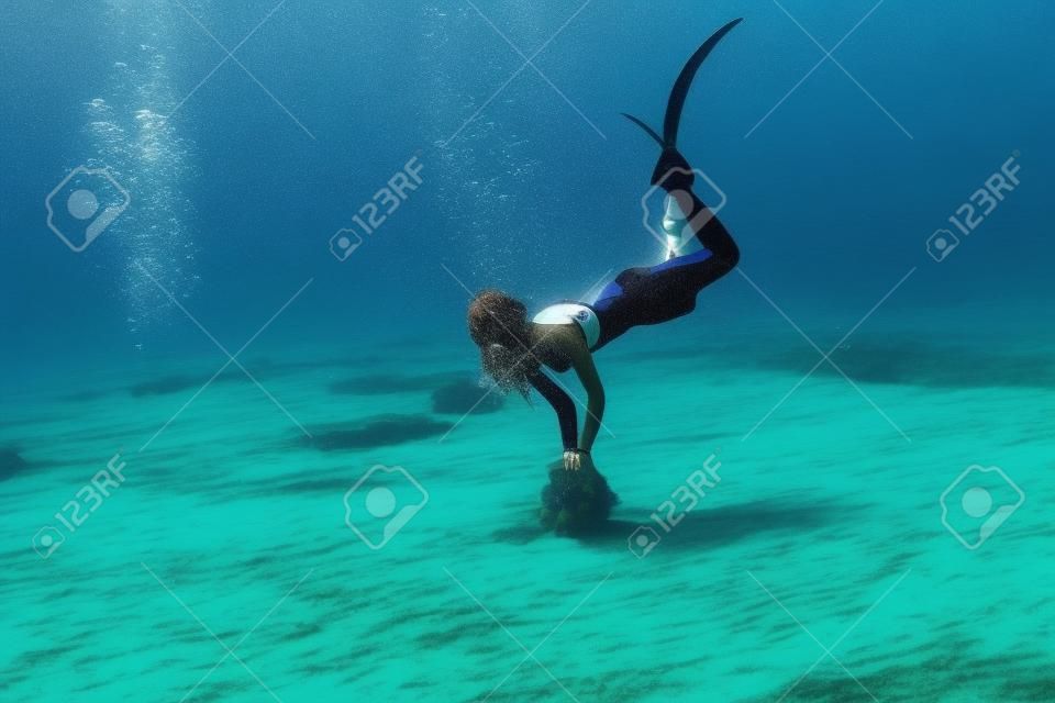 Une femme attirante d'apnéiste avec des palmes plonge au fond de l'eau en mer.
