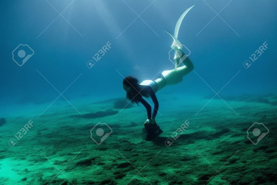 Une femme attirante d'apnéiste avec des palmes plonge au fond de l'eau en mer.