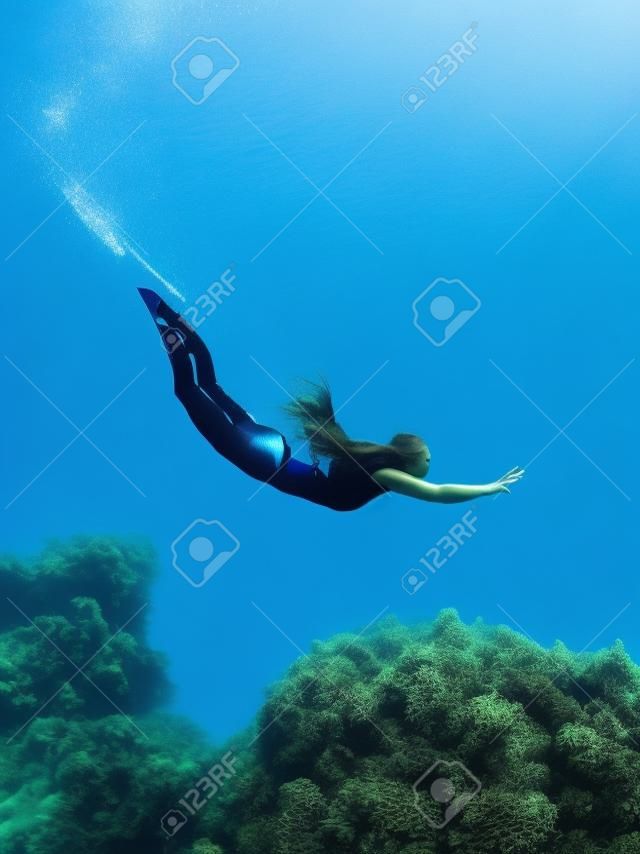 프리다이버 소녀는 프리다이빙 지느러미와 해초가 있는 바다 밑바닥을 활공합니다. 푸른 바다에서 여자와 아름다운 빛과 함께 프리다이빙