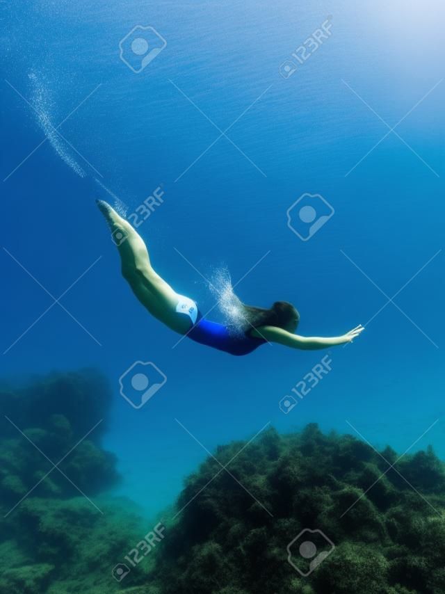 Free diver girl glides with freediving fins and sea bottom with seaweed. Freediving with woman and beautiful light in blue ocean
