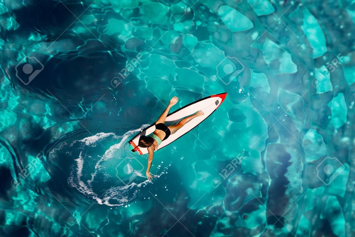 Surf girl swim with surfboard in transparent ocean. Aerial top view