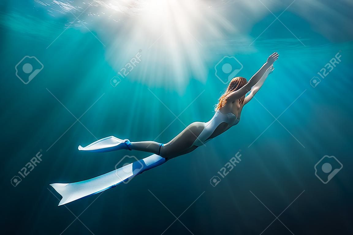 Mulher liberdiver com barbatanas brancas debaixo d'água. Freediving com linda menina no oceano e raios de sol