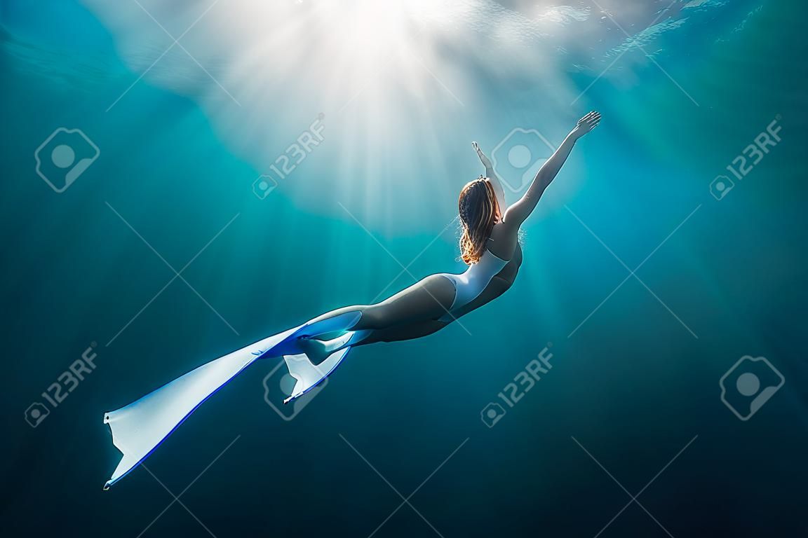 Mulher liberdiver com barbatanas brancas debaixo d'água. Freediving com linda menina no oceano e raios de sol