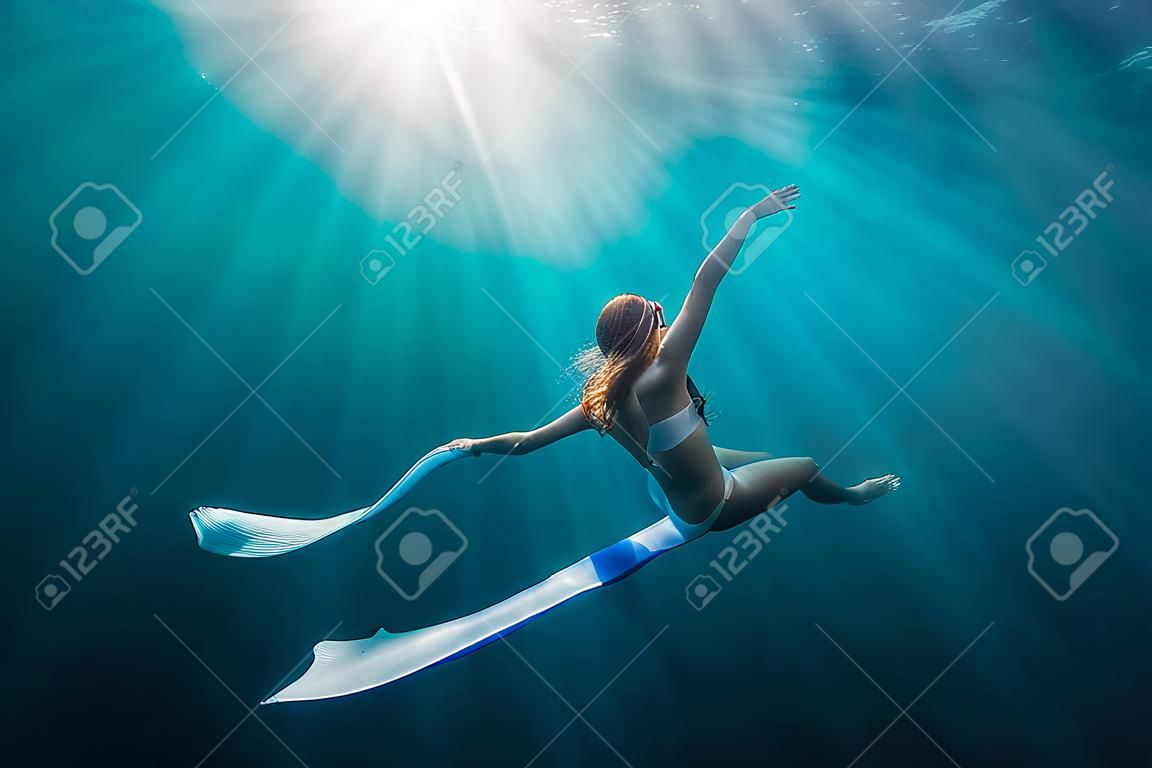 Vrouw freediver met witte vinnen onder water. Vrijduiken met mooie meisje in de oceaan en zonnestralen