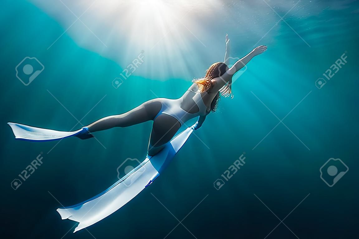 Woman freediver with white fins underwater. Freediving with beautiful girl in ocean and sun rays