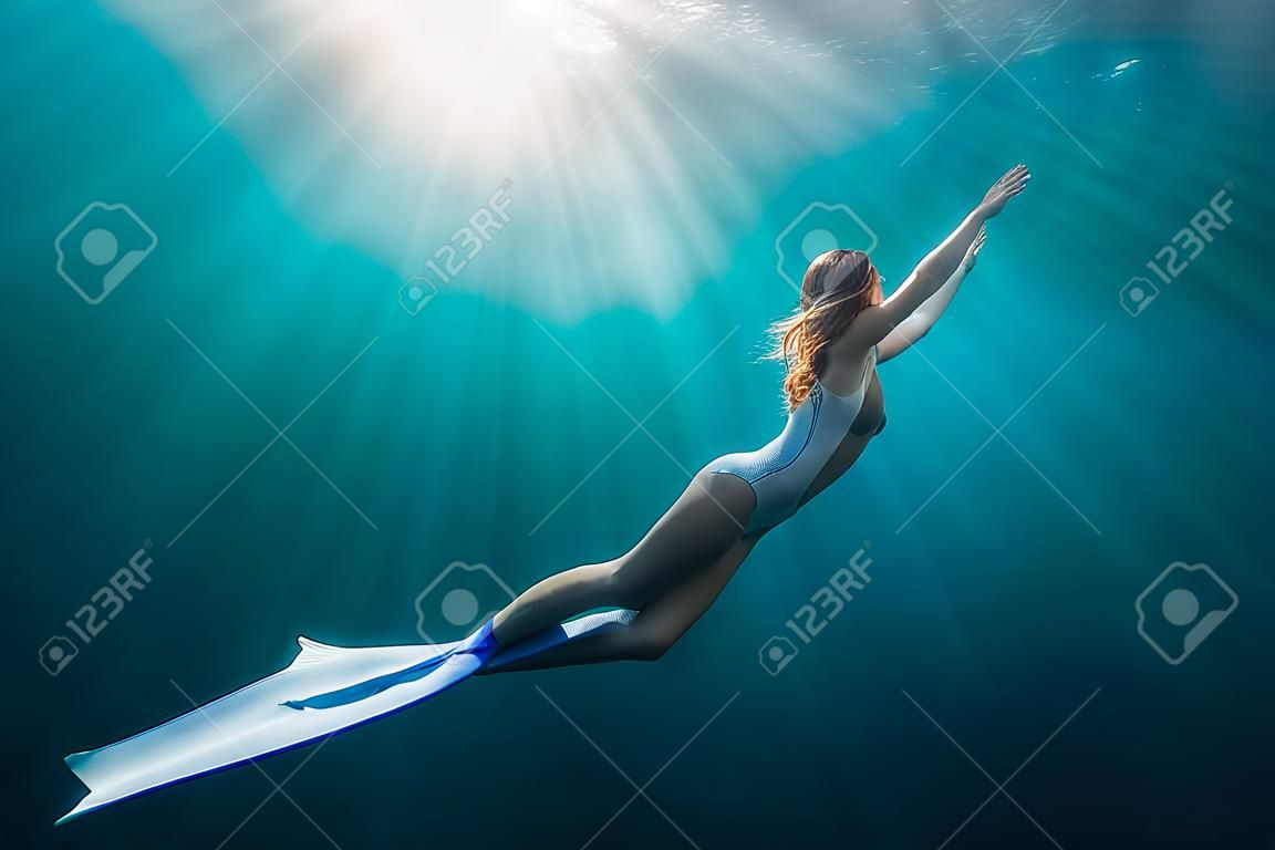 Vrouw freediver met witte vinnen onder water. Vrijduiken met mooie meisje in de oceaan en zonnestralen