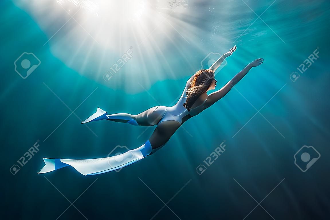 Woman freediver with white fins underwater. Freediving with beautiful girl in ocean and sun rays
