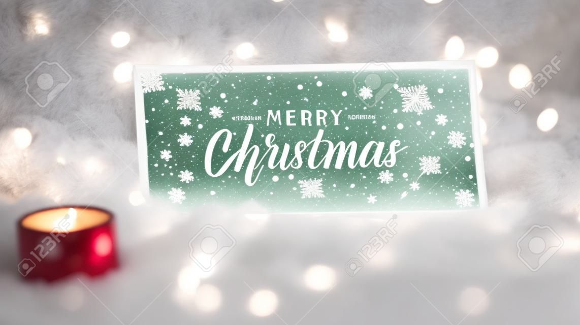 Scritta di buon natale su un cartello di vetro o vassoio su una pelliccia bianca insieme a decorazioni e luci natalizie