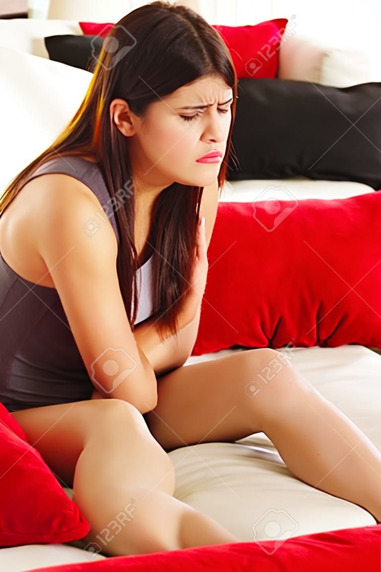 Woman having a stomachache sitting on sofa at her home 