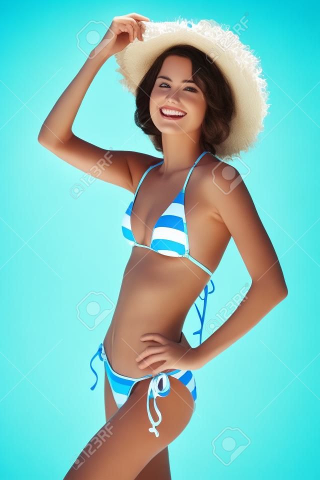 Młoda szczupła kobieta nosi strój kąpielowy i letni kapelusz.