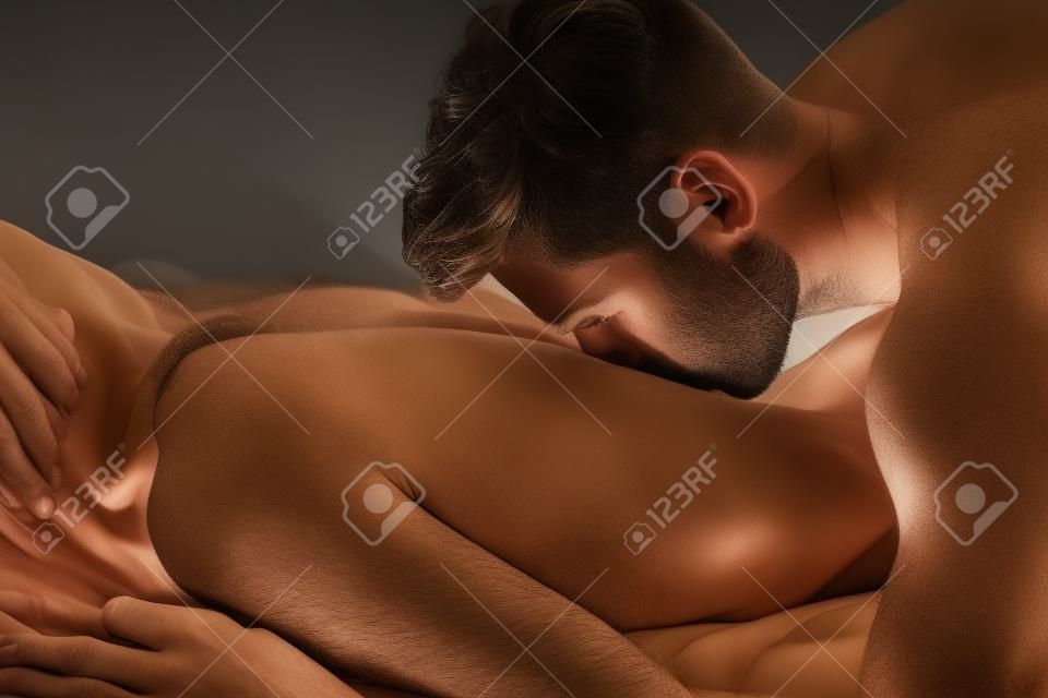 Een man die een vrouw kust in haar rug op bed.