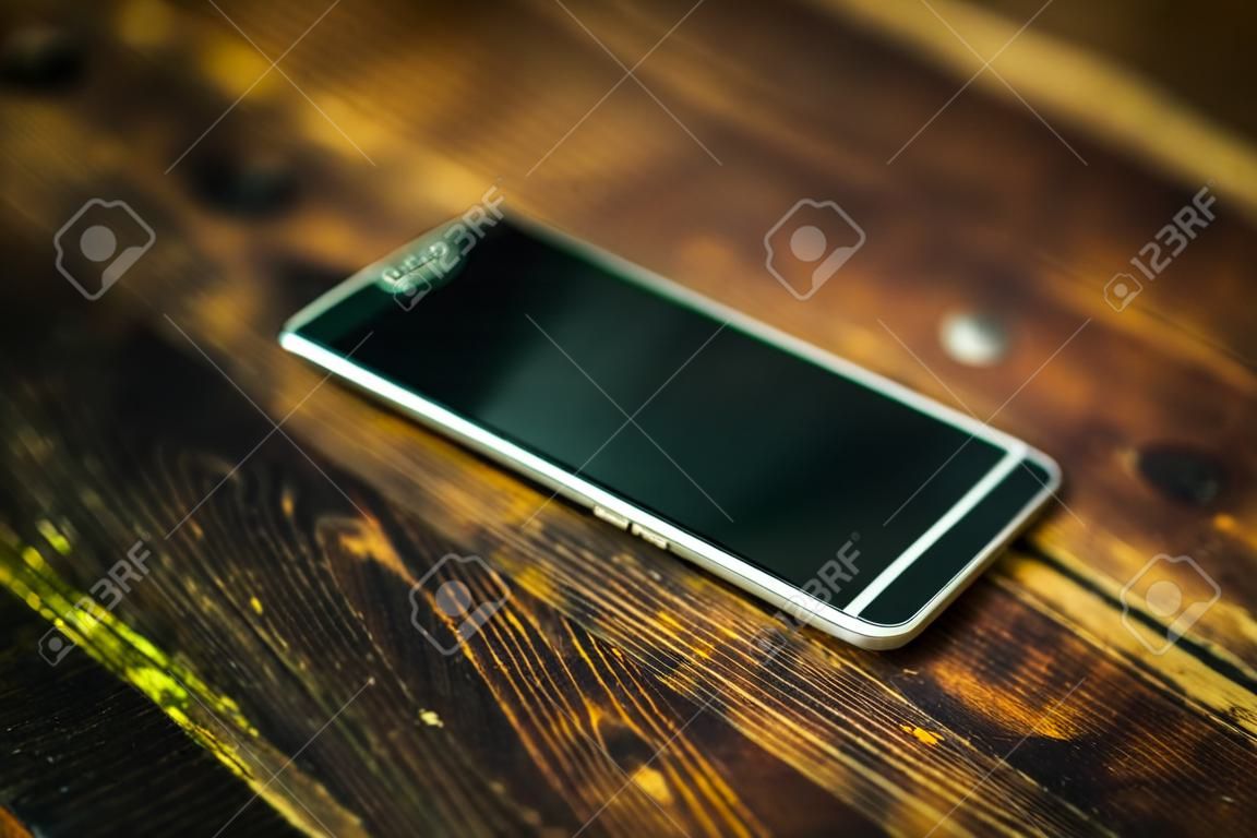 Black mobile phone on the wooden table.